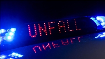 Das Blaulicht auf einem Fahrzeug der Polizei leuchtet in der Dunkelheit, während auf dem Display der Hinweis "Unfall" zu lesen ist.