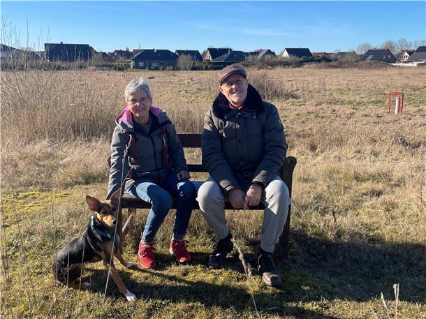 Paar mit Hund sitzt auf einer Bank.