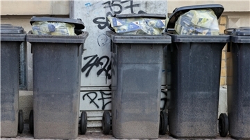 Übervolle Restmüllbehälter stehen in einer Reihe an einer Häuserwand.
