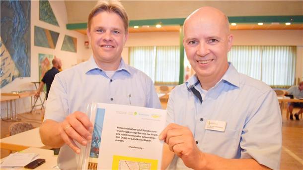 Darum sorgt die geplante Gewerbepark-Gesellschaft in Nordenham für Diskussionen Das Foto zeigt zwei Männer, die eine Studie für ein interkommunales Gewerbegebiet in der Wesermarsch in der Hand halten. Die Studie empfiehlt die Gründung einer Gewerbepark-Gesellschaft. Um sie ging es jetzt im Wirtschaftsausschuss in Nordenham.