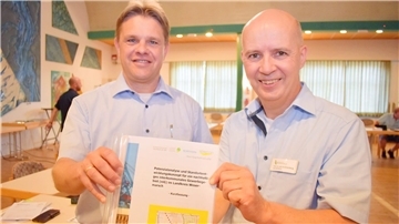 Das Foto zeigt zwei Männer, die eine Studie für ein interkommunales Gewerbegebiet in der Wesermarsch in der Hand halten. Die Studie empfiehlt die Gründung einer Gewerbepark-Gesellschaft. Um sie ging es jetzt im Wirtschaftsausschuss in Nordenham.