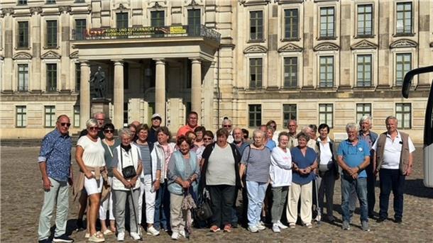Große Reisegruppe Älterer vor einem Gebäude mit historischer Fassade