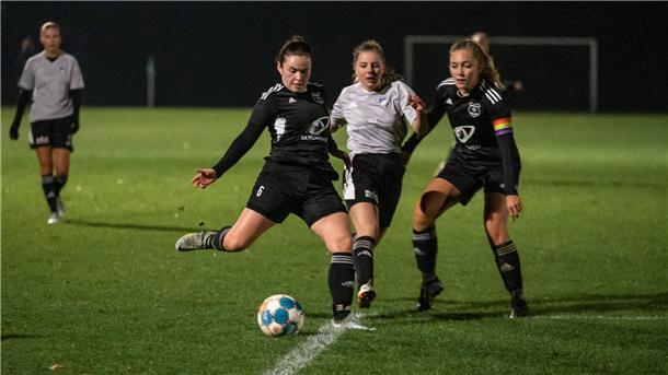 Drei Frauen in Sporttrikots laufen um einen Fußball herum.