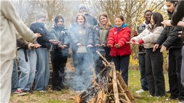 Jugendliche halten ihre Hände zum Lagerfeuer und singen.