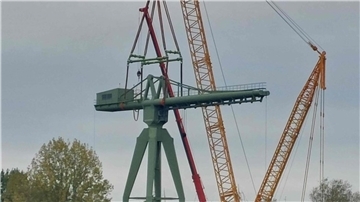 Ein gelber Raupen-Kran hebt die Kanzel des historischen grünen Krans auf das Unterteil.  