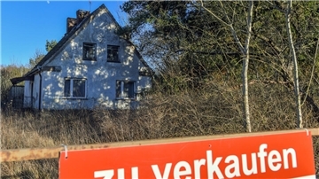 Ein Schild mit der Aufschrift «zu verkaufen» steht auf einem Grundstück mit einem Einfamilienhaus. 