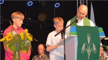 Zwei Jungen mit einem Pastor auf der Bühne.