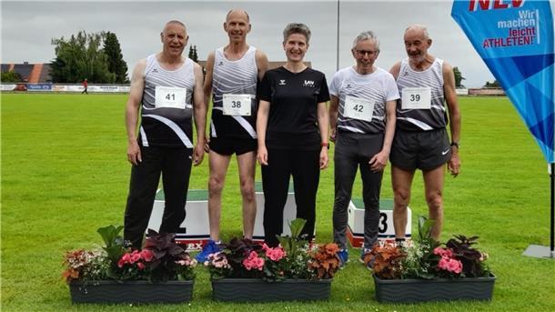 Sechs Landesmeistertitel für Senioren-Team der LAV Zeven Vier Männer in weißen Trikots und eine Frau in schwarze, Trikot stehen auf einem Rasen und haben drei Blumenkästen vor ihren Füßen.