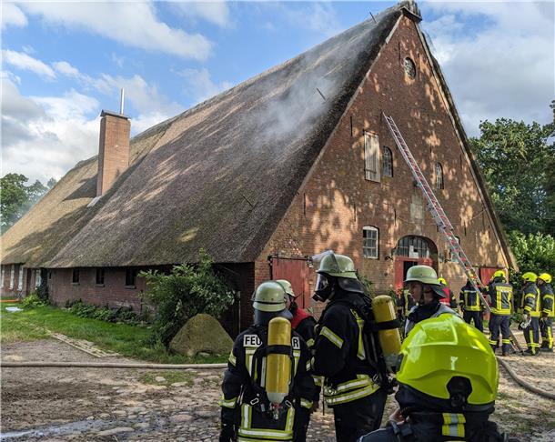 Rund 120 Einsatzkräfte halten Brand eines Reetdachhauses in Wittstedt in Schach Mehrere Gruppen von Feuerwehrleuten vor einem Reetdachhaus. Eine lange Leiter lehnt an der Wand des Gebäudes.
