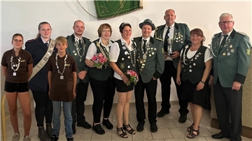 Mehrere Menschen stehen mit Orden und Blumen vor einer Vereinsfahne. 