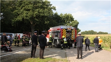 Ein Feuerwehrfahrzeug steht am Rand eines Feldes. Drumherum sind Feuerwehrleute aktiv.