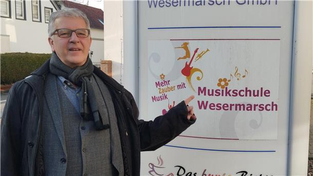 Mann mit Jacke und Schal steht neben Infostele in Brake.