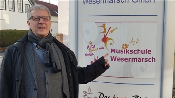 Mann mit Jacke und Schal steht neben Infostele in Brake.