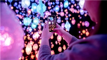 Eine Frau fotografiert mit ihrem Handy die leuchtende Rauminstallation.