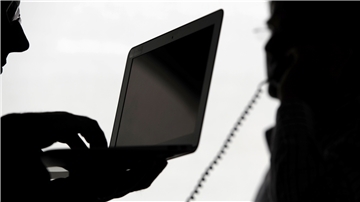 Zwei Männer stehen mit Computer und Telefon vor einem Fenster. Das Bild symbolisiert das Thema Telefonüberwachung.