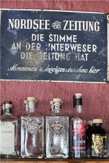 Ein Schild hängt über Glasflaschen, die auf einem Regal stehen, an der Wand.