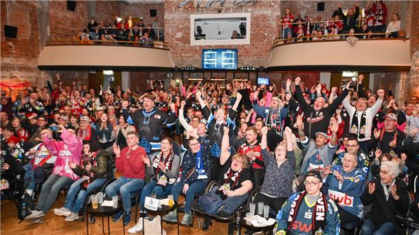 Eishockey-Fans schauen gemeinsam ein Spiel auf einer Leinwand und fiebern mit. 
