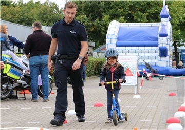 Ein Polizist begleitet ein Mädchen bei einer Mitmachaktion.