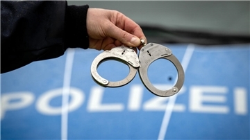Ein Polizist hält vor einem Polizeiauto Handschellen in den Fingern.