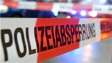 Ein Flatterband mit der Aufschrift „Polizeiabsperrung“ ist an einem Einsatzort vor einem Feuerwehrfahrzeug mit Blaulicht zu sehen. 