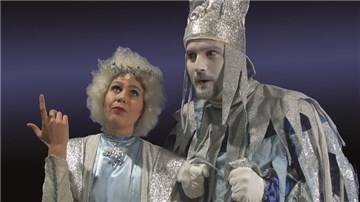 Zwei Schauspieler in silberfarbenen Kostümen stehen auf einer Bühne. 