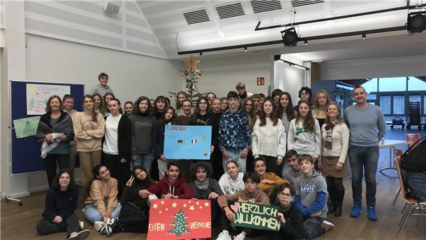 Teenager stehen für ein Gruppenbild in einem Raum. Die vordere Reihe sitzt. Es werden Schilder mit deutschen und französischen Texten zu Weihnachten hochgehalten.