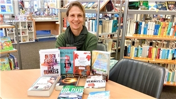 Eine Frau sitzt in der Stadtbücherei Nordenham an einem Tisch und präsentiert dort einige Bücher.