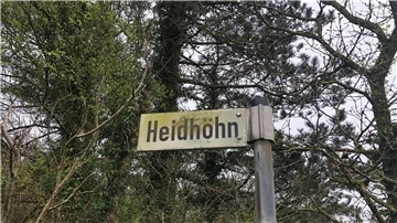 Ein Straßenschild mit der Beschriftung "Heidhöhn" vor einigen Bäumen
