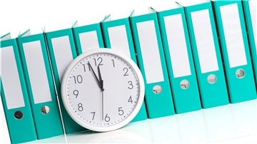 Eine Uhr vor türkisfarbenen Ordnern.