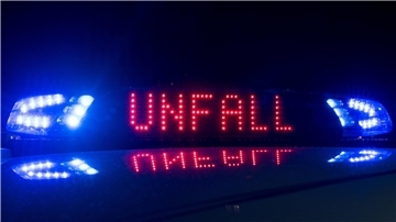 Das Blaulicht auf einem Fahrzeug der Polizei leuchtet in der Dunkelheit, während auf dem Display der Hinweis "Unfall" zu lesen ist.