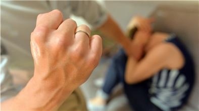 Eine Faust wird bedrohlich neben einer zusammengekauerten Frau erhoben.