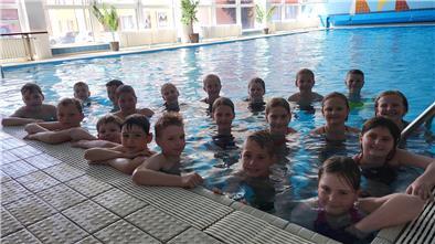 Dutzende Kinder stehen am Beckenrand eines Schwimmbeckens und lächeln in die Kamera. 