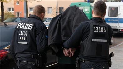 Zwei Polizisten führen einen Mann in Handschellen ab.
