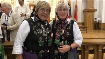 Zwei Frauen in einer Tracht stehen vor einem Altar.
