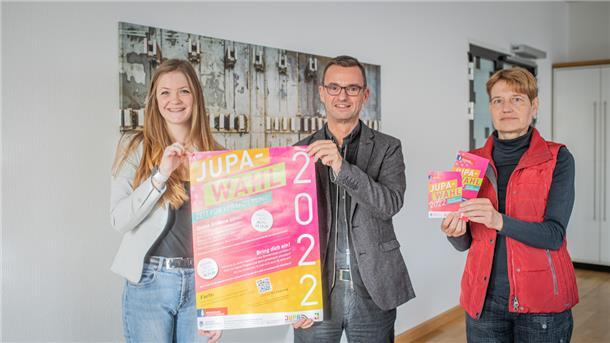 Drei Menschen halten Werbung für das Jugendparlament in die Kamera.