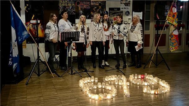Frauen singen in einem Kulturzentrum Lieder, während vor ihnen - mit Teelichtern gebildet -die Zahl 679 zu sehen ist.