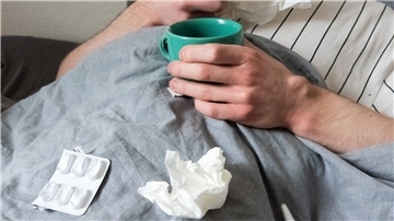  Ein Mann liegt mit Taschentüchern, Teetasse, Nasenspray und Tabletten im Bett (gestellte Szene). 