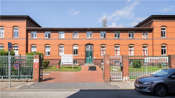 rotes Backsteingebäude mit grüner Tür in einer parkähnlichen Anlage 