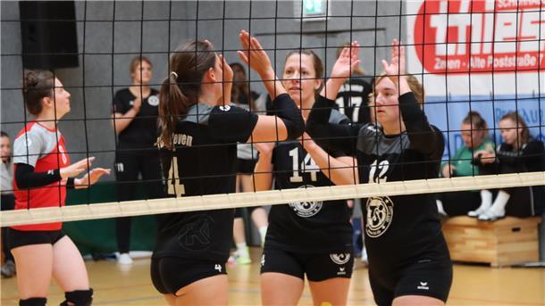 Hinter einen Volleyballnetz klatschen sich drei Frauen gegenseitig ab.