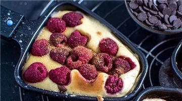 Raclette-Pfännchen mit Pfannkuchen-Teig und Himbeeren.