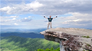 Ein Mann steht auf einem überlappenden Felsen.