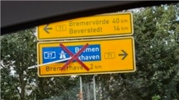 Ein gelb-schwarzes Schild, auf dem die Begriffe "Bremerhaven", "Beverstedt" und "Bremervörde" stehen. Über den Abschnitt "Bremerhaven" ist ein rotes Kreuz gelegt.