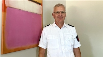 Ein Polizeibeamter steht neben einem abstrakten Gemälde und lächelt in die Kamera.