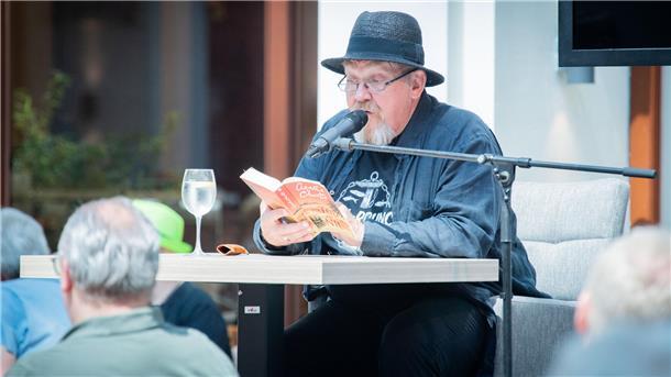 Mann sitzt am Tisch und liest aus einem Buch. 
