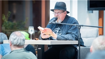 Mann sitzt am Tisch und liest aus einem Buch. 