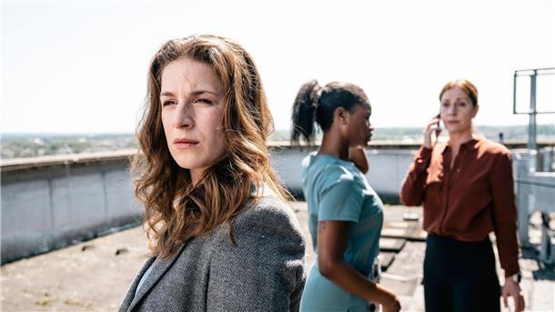 Dina Schwarz (Lou Strenger, links) blickt zu dem am Dach-Rand stehenden Nathan Freye. Im Hintergrund rufen Veronika Jelinek (Ulrike Tscharre, rechts) und Jenny de Luca (Melodie Simina, Mitte) Hilfe.