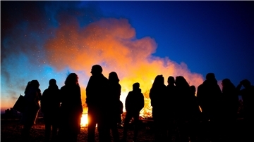 Menschen stehen vor einem Osterfeuer bei abendlichem Himmel.