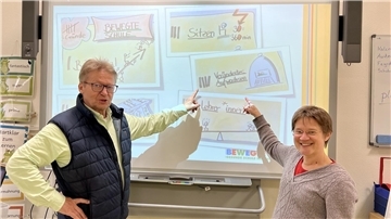 Ein Mann und eine Frau zeigen auf ein Smartboard