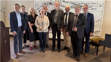 Gruppenfoto von neun Personen bei der Verleihung des Hermann-Allmers-Preises 2025 in der Burg Bederkesa. In der Mitte steht Preisträger Hans Gerhard Steimer, umgeben von Vertreterinnen und Vertretern aus Kultur, Verwaltung und Jury. Im Hintergrund ist eine Zeichnung einer historischen Landschaft zu sehen.