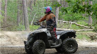 Eine Frau steht in dreckiger Kleidung auf einem dreckigen Quad.